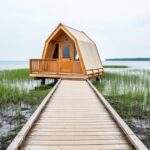 “oTENTik A-frame cabin near a wooden boardwalk through marsh reeds with Lake Erie visible in the background at Point Pelee National Park.”