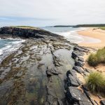Panoramic coastal landscape in New Brunswick showing Fundy’s rocky tidal shoreline and cliffs next to Kouchibouguac’s sandy dunes and salt-marsh grasses.