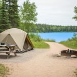 A tent and picnic setup at a Riding Mountain National Park campsite near a forest and lake shoreline.